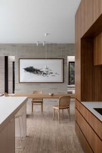 Modern kitchen with a concrete backsplash, wooden furniture, and a white pendant light hanging above the dining table.