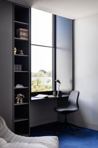 Modern minimalist home office with a built-in desk, black metal chair, and large window.