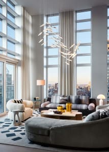 A modern living room with a city view, featuring a chandelier, sofas, and a coffee table.