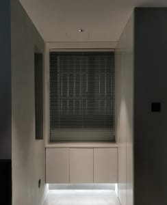 Modern, minimalist residential interior featuring metallic blinds and white cabinet storage.