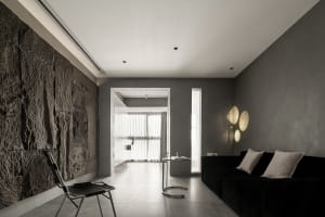 A minimalist residential interior featuring polished concrete walls, a black sofa, and modern lighting.