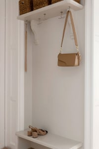 A minimalist white storage space with a bench, hooks, and a bag hanging.