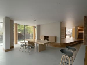 A modern living room with a wooden dining table and chairs next to a kitchen area with a bar in a contemporary home design.