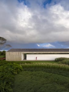A modern house with green packgrass in the foreground and a cloudy sky above.