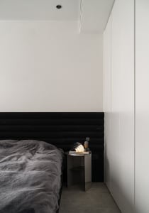 A modern minimalist bedroom featuring a black upholstered bed and a metallic bedside table with a modern lamp.