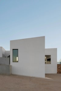 A minimalist modern house with white walls and geometric shapes, featuring a small rectangular window.
