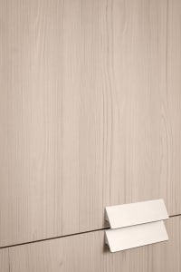 A close-up view of a modern minimalist wooden cabinet with a simple metallic handle
