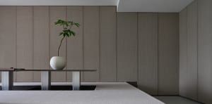 A minimalist interior with textured fabric walls and a sleek table holding a vase with a single plant.