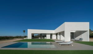 Modern residential exterior with white concrete walls and a swimming pool.
