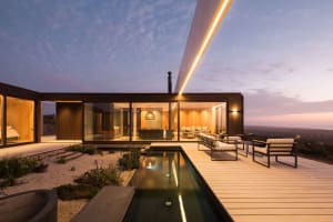 Modern residential house with a wooden exterior, large windows, and lighting features during twilight.