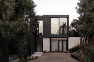 Modern house exterior featuring black aluminum panels and large glass windows surrounded by greenery.