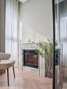 A modern living room with a marble fireplace, contemporary chair, and green plant.