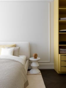 Minimalist bedroom featuring a white bed with textured bedding, a white side table with a wooden elephant figurine, and a yel