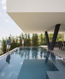 A modern swimming pool with concrete walls and a covered patio area.