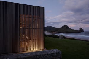 A minimalist architectural exterior made of wood at dusk with a coastal view.
