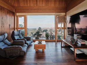 modern living room with wooden furniture and floor, large window showcasing outdoor scenery