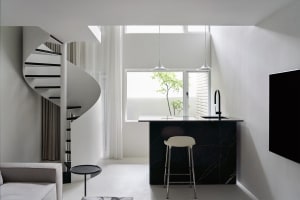 A modern minimalist living space featuring a spiral staircase, a bar with a black marble countertop, and a TV.
