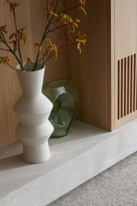 Modern empty space featuring a wooden cabinet and ceramic vase with flowers.