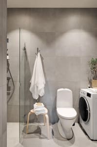 A modern minimalist bathroom with concrete walls, a glass-enclosed shower, a white toilet, a laundry machine, and a small woo