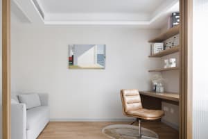 A minimalist home office with a beige leather chair and a desk, featuring a wooden floor and minimalist decor.