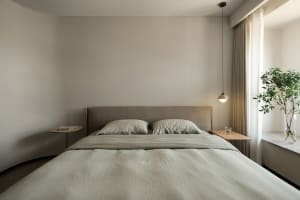 Neutral-toned minimalist bedroom with a bed, pillows, and a single hanging light fixture