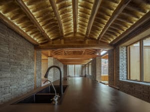 Modern kitchen interior featuring wooden beams, brick walls, and concrete countertops.
