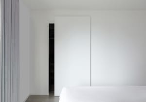 A minimalist bedroom with a white wall, bed, and sliding door.