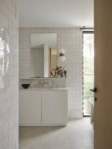 Modern bathroom with marble tiles, white cabinetry, and a sink with brass fixtures.