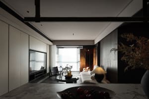 A modern living room with minimalist furniture, dark accents, and large windows.