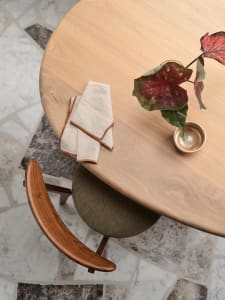 Modern round wooden table with a wooden napkin, a ceramic vessel with a plant, and a terrazzo floor.