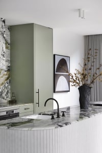 A modern minimalist kitchen features a white and green marble countertop, with a black faucet and contemporary green cabinetr