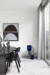 A modern minimalist dining room featuring black furniture, a geometric abstract painting, and decorative vases.