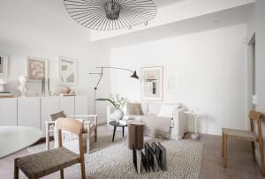 A modern minimalist living room with neutral-toned furniture and decor, featuring a white sofa, wooden chairs, and a black an