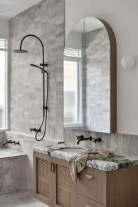 A modern bathroom featuring marble countertops and concrete elements, with an arched mirror above the vanity.