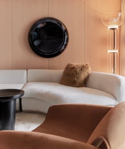 A modern living room with a curved white sofa, brown armchair, and a black round mirror on the wall.