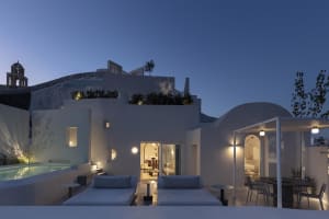 Modern residential patio with white plaster walls and night lighting, featuring a sitting area with lounge chairs and a dinin