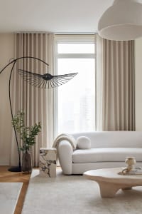 A modern, minimalist living room with a white sofa, neutral curtains, and a sleek, metal floor lamp.