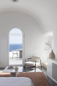 A minimalist living room with white walls and furniture, featuring a comfortable lounge chair with a cushion, a small round t