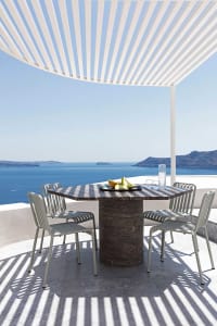 Stone table with metal chairs under a pergola on an outdoor terrace overlooking the sea.