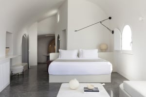Modern minimalist bedroom featuring white elements, including a bed with white bedding, a white table, and a white chair, wit