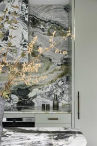 Modern kitchen with marble walls, countertops, and sink, featuring stainless steel appliances and green plants.