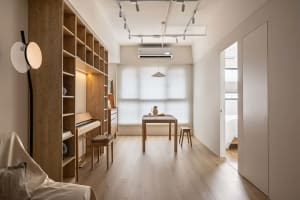 A minimalist living room with wooden furniture and flooring, featuring a large bookshelf, a table, and a piano.