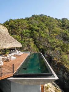 Modern concrete swimming pool overlooking dense green hillside