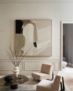 A modern living room with beige walls, minimalist furniture, and abstract artwork on the wall.