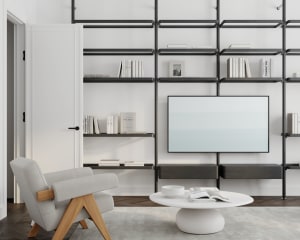 A modern living room featuring a white armchair, a circular white coffee table with a white bowl and magazines, and a wall-mo