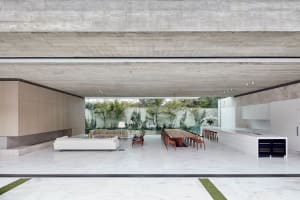 Contemporary living area with white marble flooring, concrete ceiling beams, and a view of an outdoor garden with greenery.