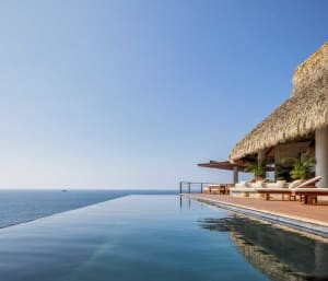 Poolside villa with thatched roof overlooking the ocean.