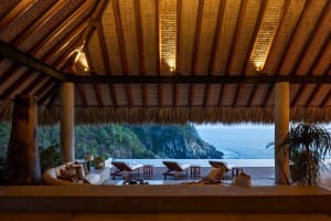 Thatched-roof pavilion overlooking a scenic ocean view with lounge chairs and a swimming pool.