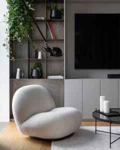 A sleek, white, textured-fabric accent chair in a minimalist living room with a modern design, featuring a black shelving uni