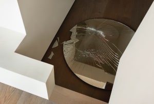 A broken circular mirror on a hardwood floor in a minimalist house.
